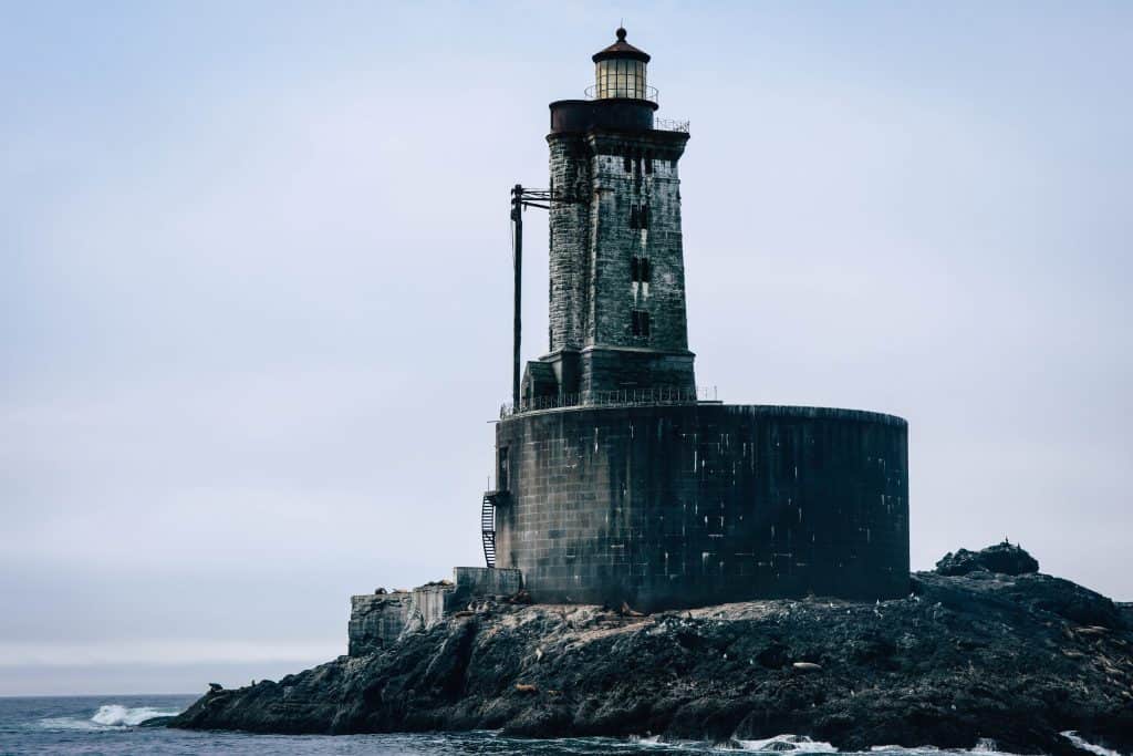 Old lighthouse on rocky seaside under cloudy sky